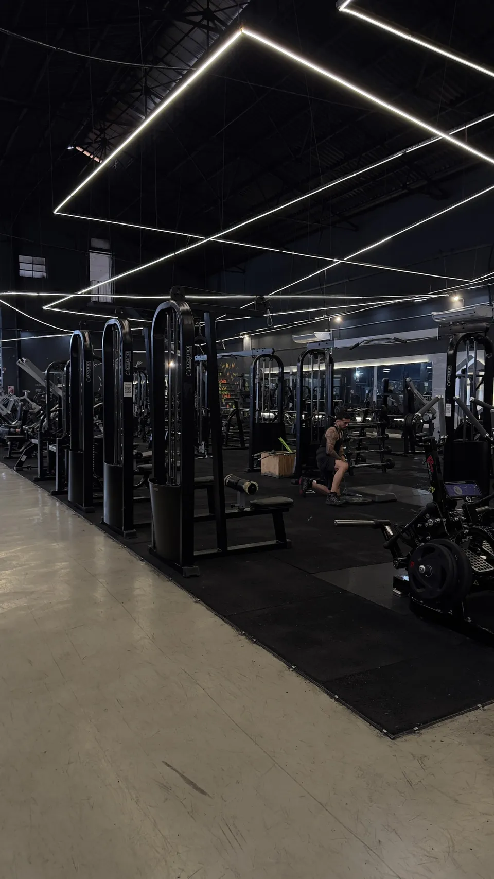 Gimnasio en penumbra con líneas de luz en el techo y las máquinas alineadas contra la pared